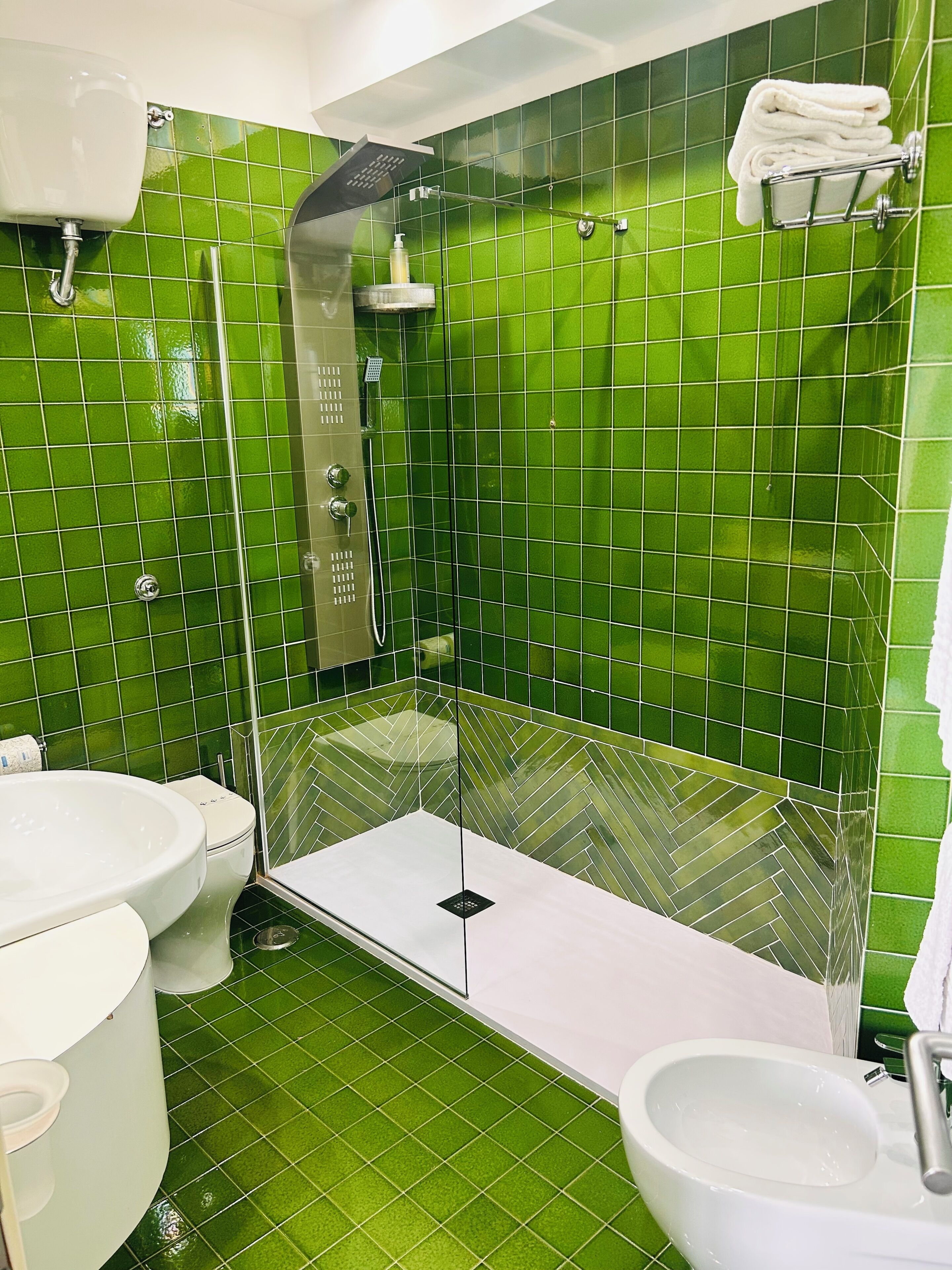 A bathroom with green tiles, a shower, a toilet, and a sink.