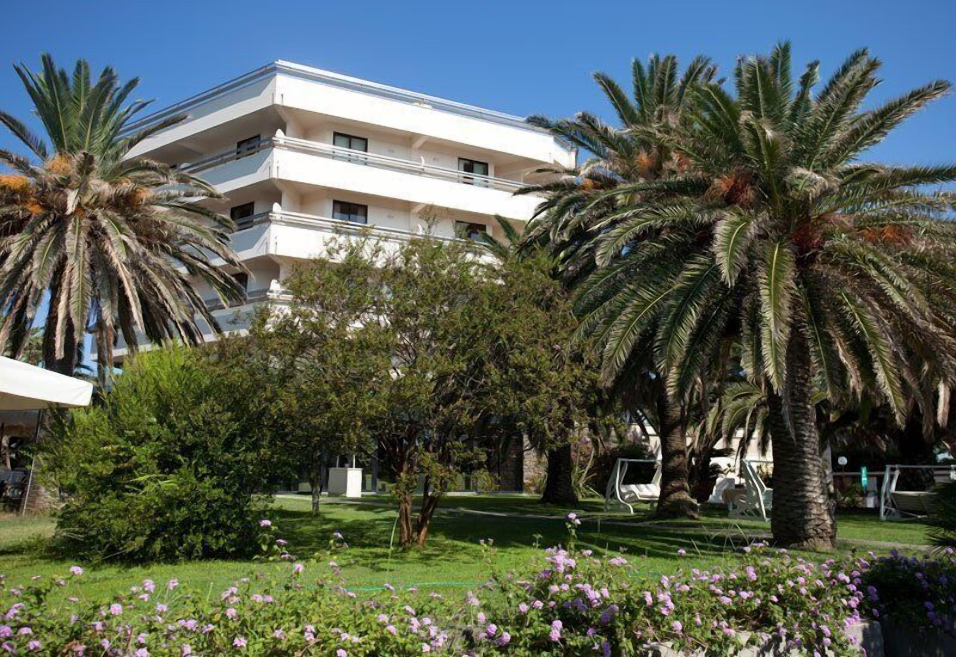 Un hôtel à plusieurs étages, doté d’une façade blanche, entouré d’une végétation luxuriante et de palmiers.