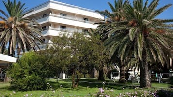 Un hôtel à plusieurs étages, doté d’une façade blanche, entouré d’une végétation luxuriante et de palmiers.