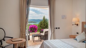 Habitación de hotel con cama, una mesita, una silla y vistas al mar y a las montañas.