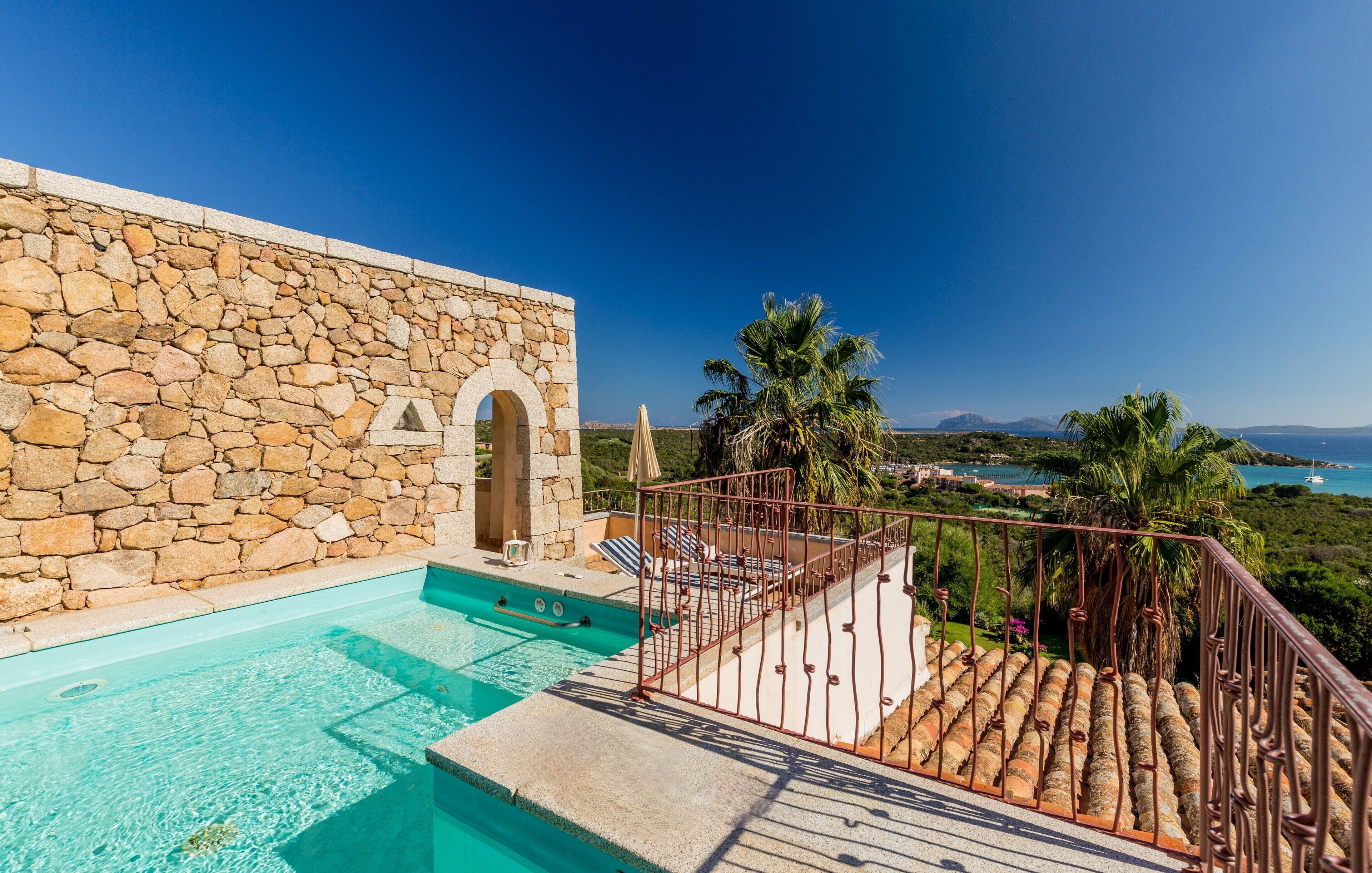 A stone building with a swimming pool, a metal railing, and a view of the sea.
