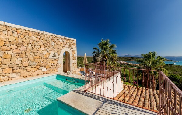 A stone building with a swimming pool, a metal railing, and a view of the sea. - Hotel Petra Bianca (Arzachena)