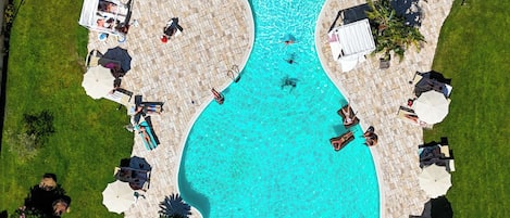 An aerial view of a swimming pool with a guitar-shaped design, surrounded by lounge chairs and umbrellas.