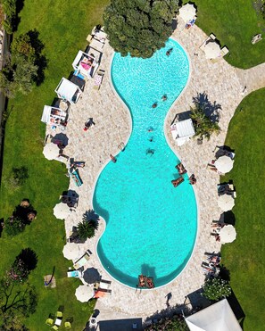 Vista aérea de una piscina con diseño en forma de guitarra, rodeada de sillas de descanso y sombrillas.