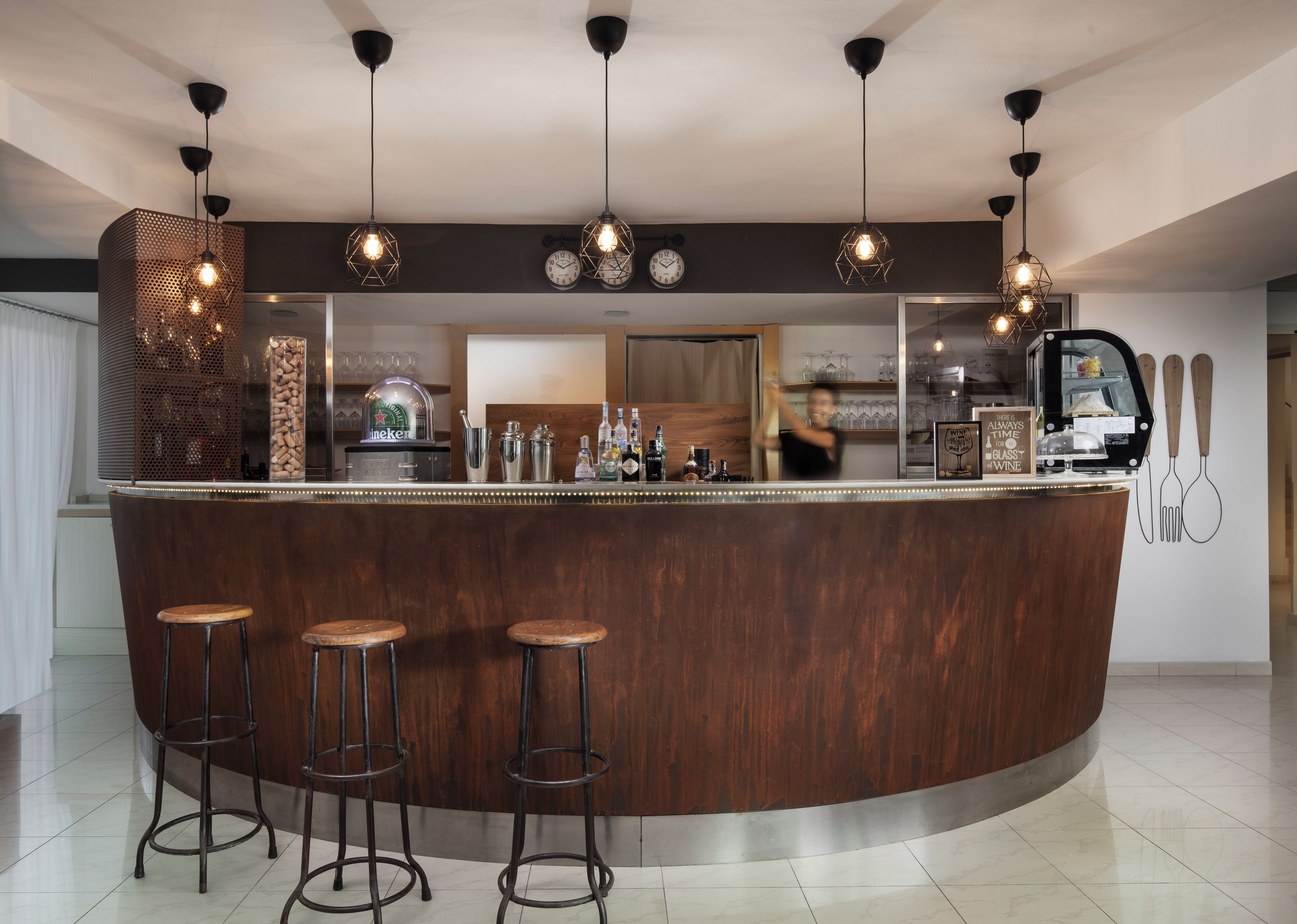 A bar area with a wooden counter, bar stools, hanging pendant lights, and a clock on the wall.