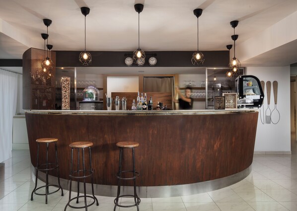 Zona de bar con mostrador de madera, taburetes, lámparas colgantes y un reloj en la pared.