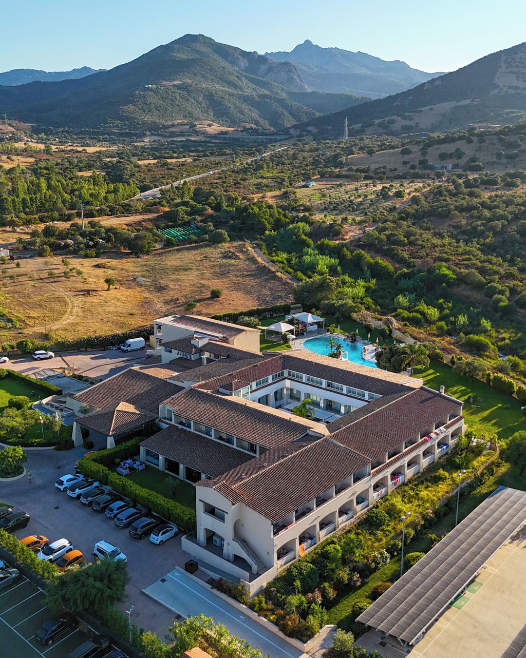Un hotel de varios pisos con piscina, rodeado de vegetación y montañas.
