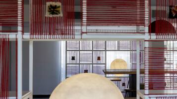 A room with a large round table, a bookshelf, and a window with blinds.