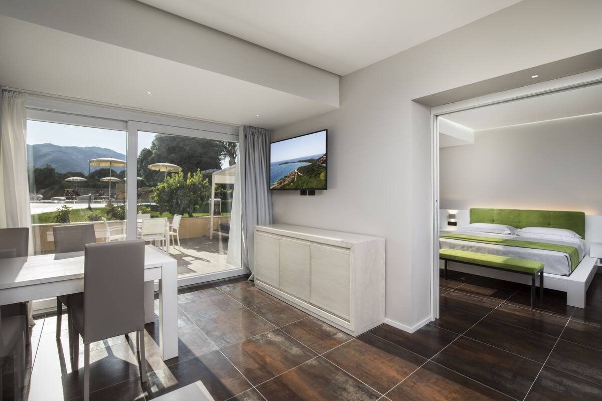 Ein modernes Hotelzimmer mit großem Fenster, einem Bett, einem Schreibtisch und einem Fernseher.