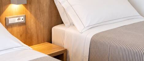 A hotel room with two beds, a wooden headboard, a bedside table, and a wall-mounted light fixture.