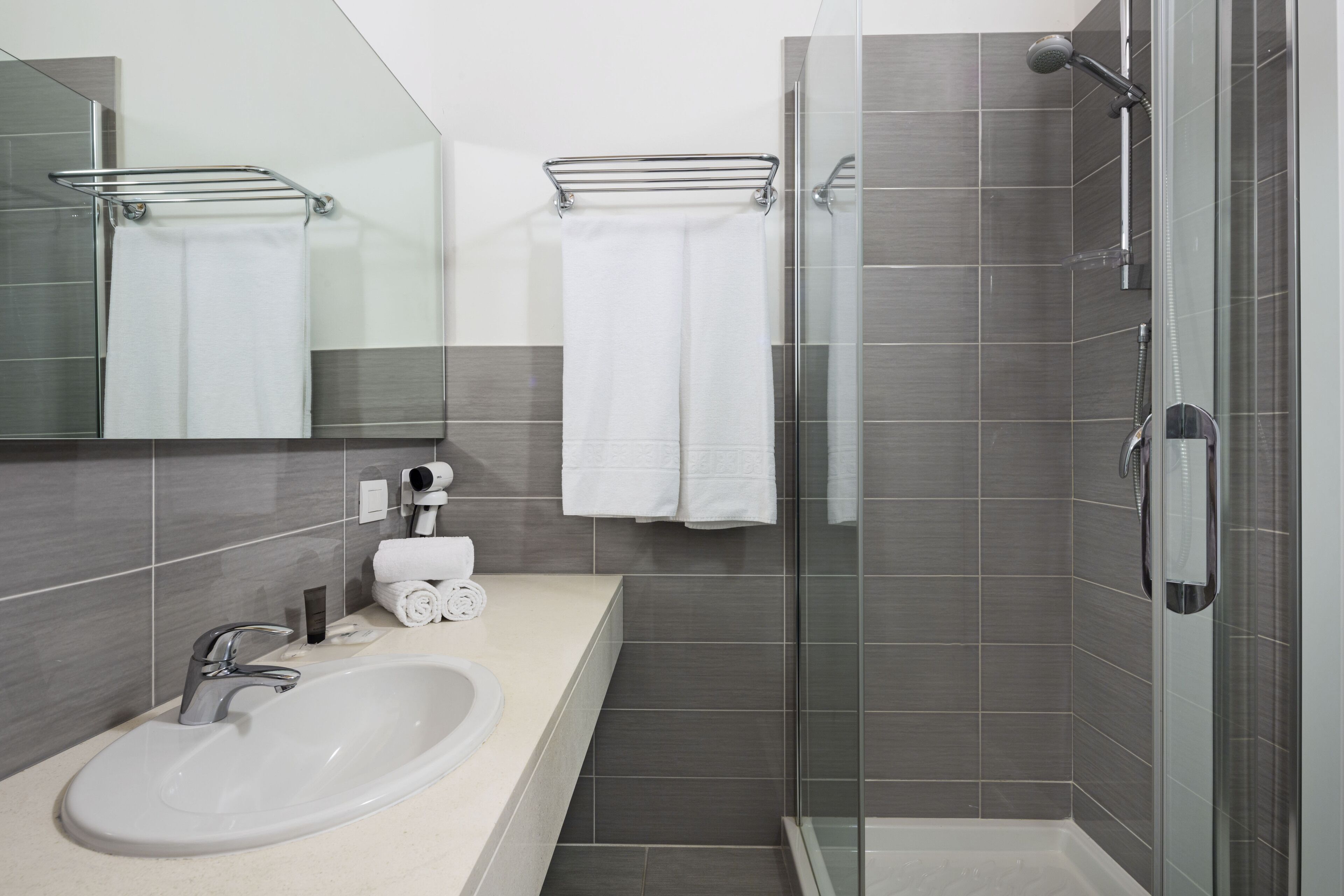 Un baño moderno con cabina de ducha de vidrio, un lavamanos blanco y un perchero para toallas.