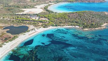 Une vue aérienne d’une zone côtière, avec des eaux turquoise limpides, des plages de sable et un paysage montagneux en arrière-plan.