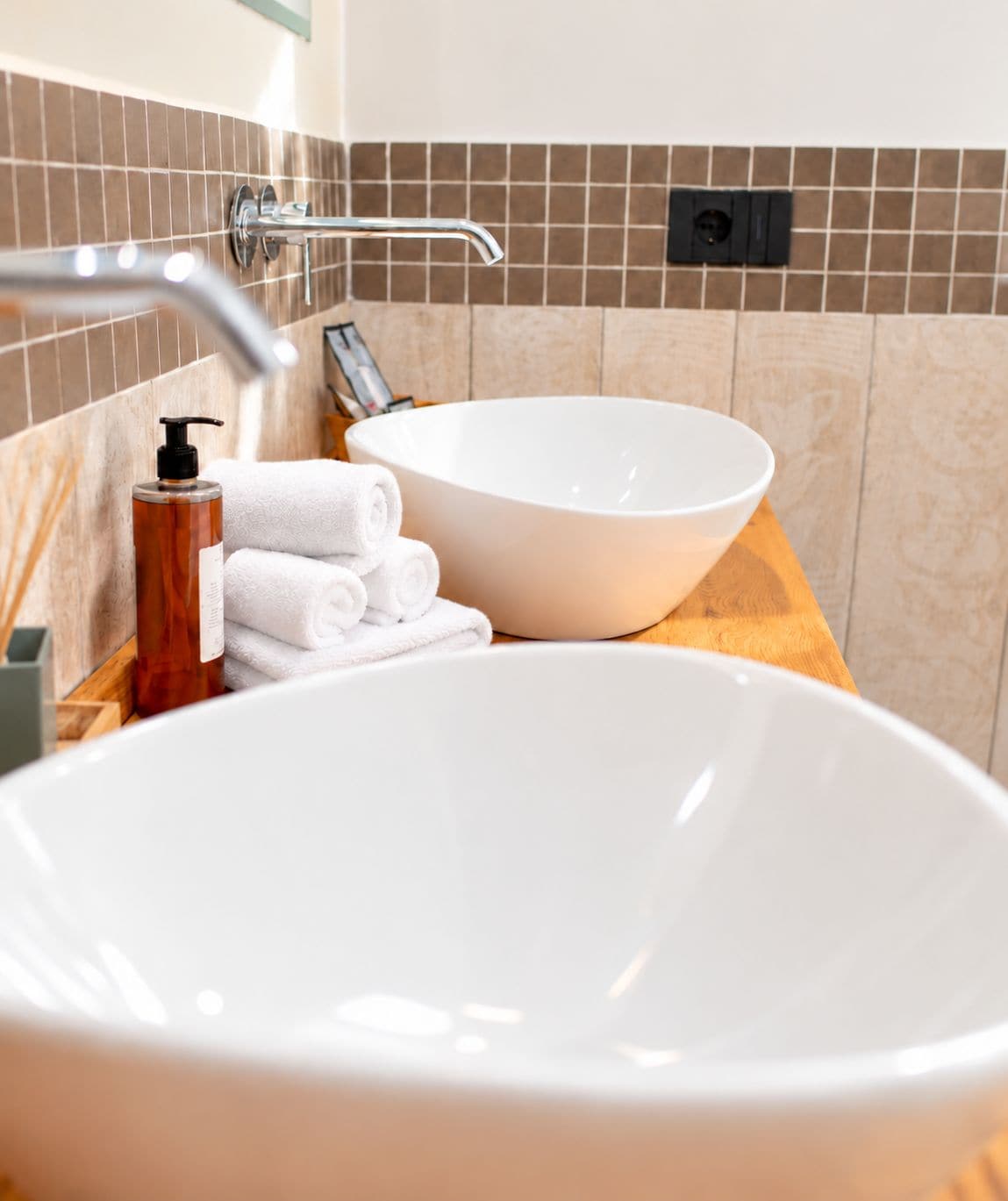 A bathroom with a white vessel sink, a wooden countertop, a towel dispenser, and a towel rack.