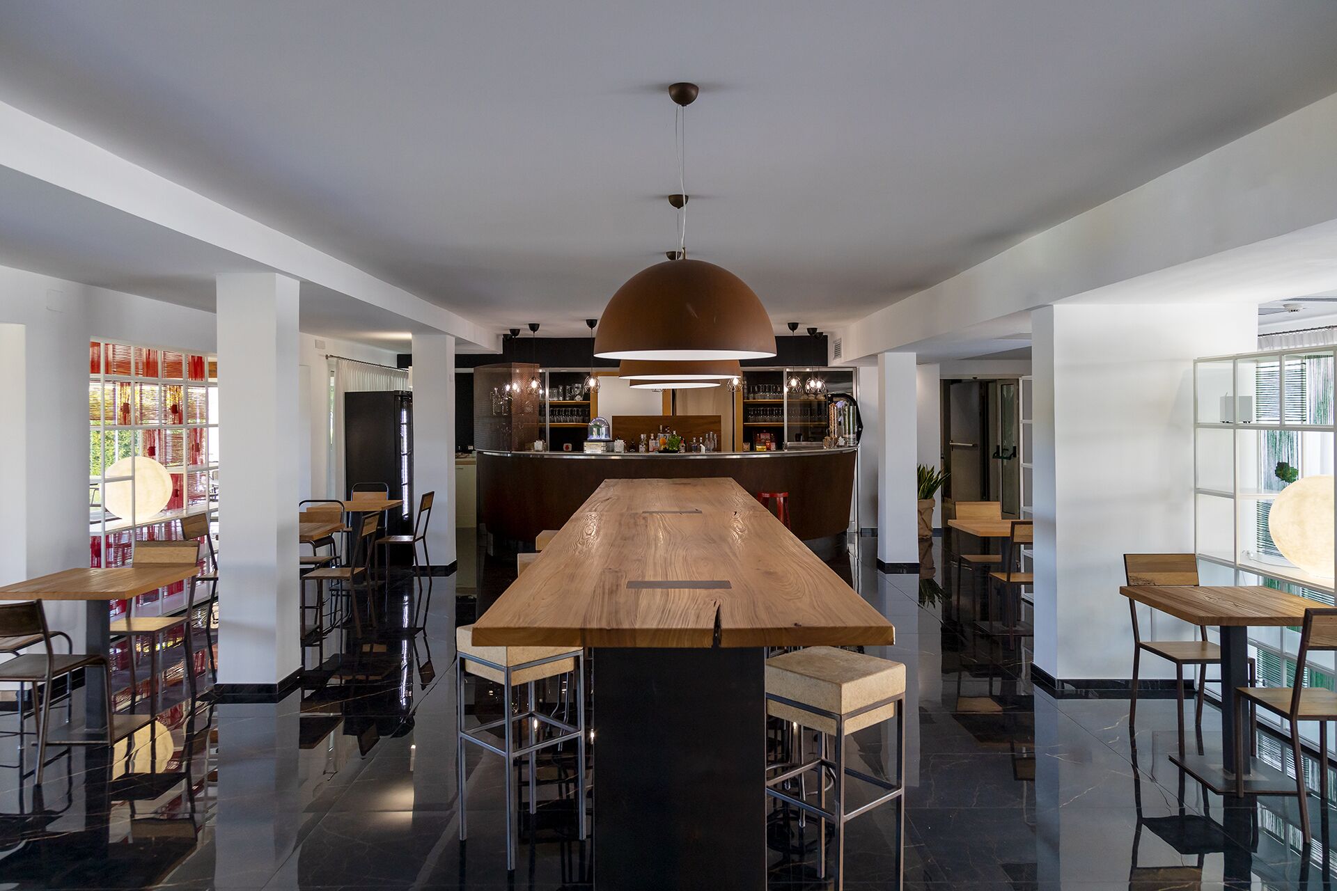 A modern bar area with a central wooden bar, multiple seating options, and a large hanging light fixture.