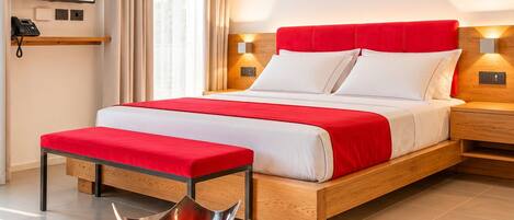 A hotel room with a bed, bedside tables, a TV, and a view of a beach.