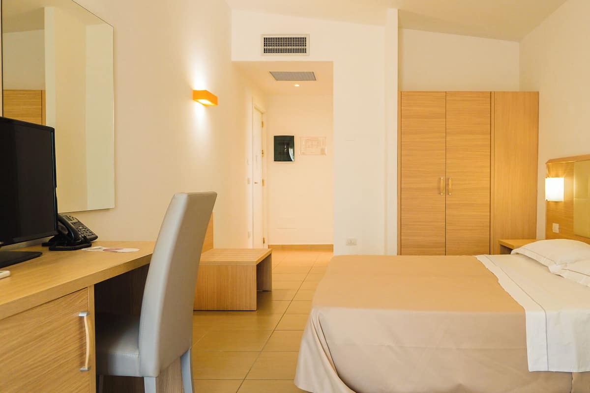 Ein Hotelzimmer mit Bett, Schreibtisch mit Computer und Telefon, Stuhl, Kleiderschrank und Spiegel.