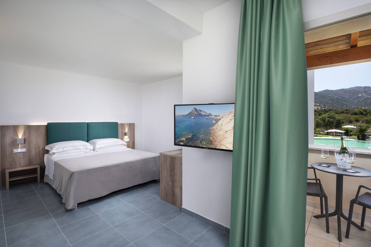 Ein modernes Hotelzimmer mit Bett, Fernseher und einem Balkon mit Blick auf den Pool.