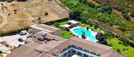 A multi-story hotel with a swimming pool, surrounded by green lawns and a hilly landscape.