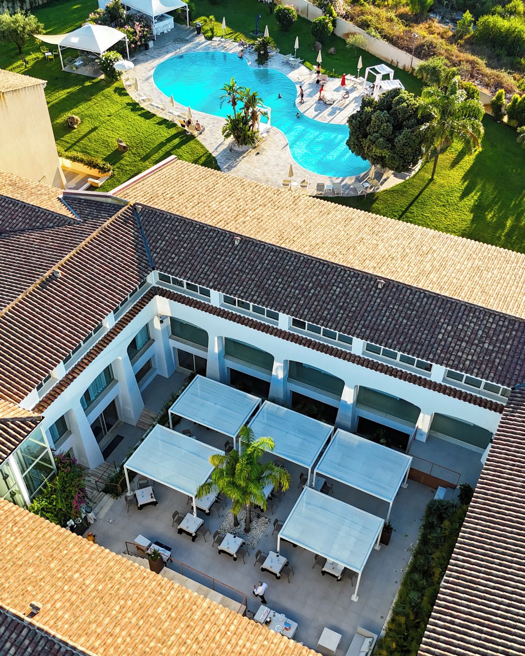 An aerial view of a hotel with a rooftop pool, outdoor seating area, and a covered patio.