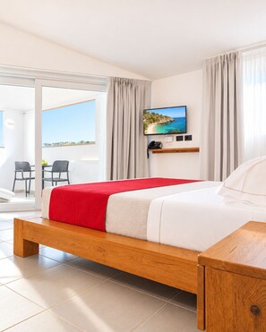 Habitación de hotel con cama, mesita de noche, televisor montado en la pared y balcón con vistas.