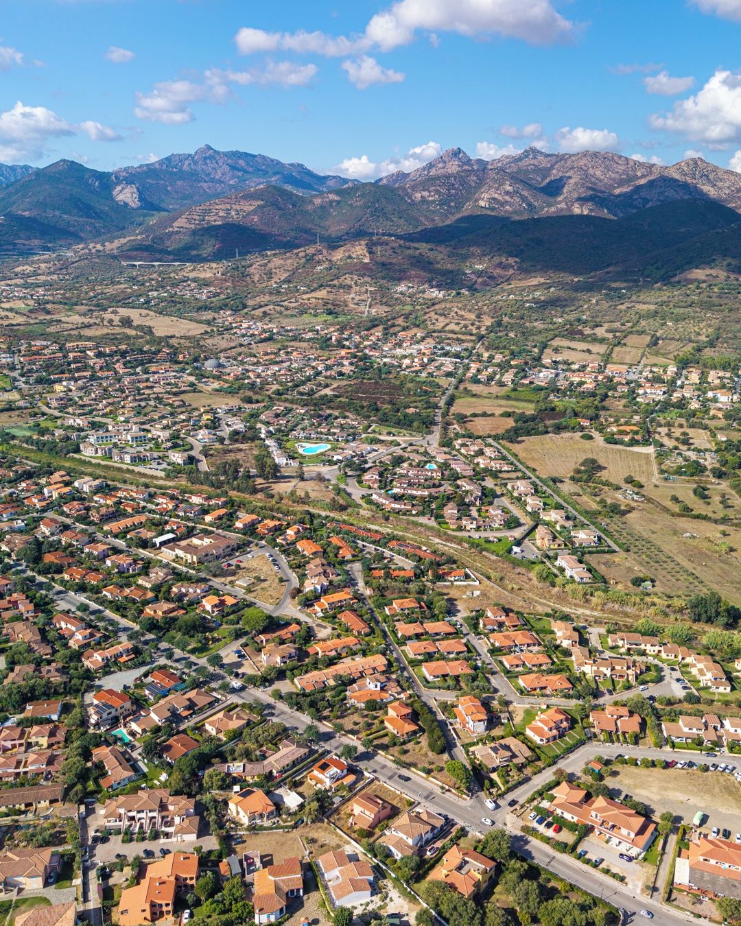 Vue aérienne d’un quartier résidentiel avec des maisons, des routes et une chaîne de montagnes en arrière-plan.