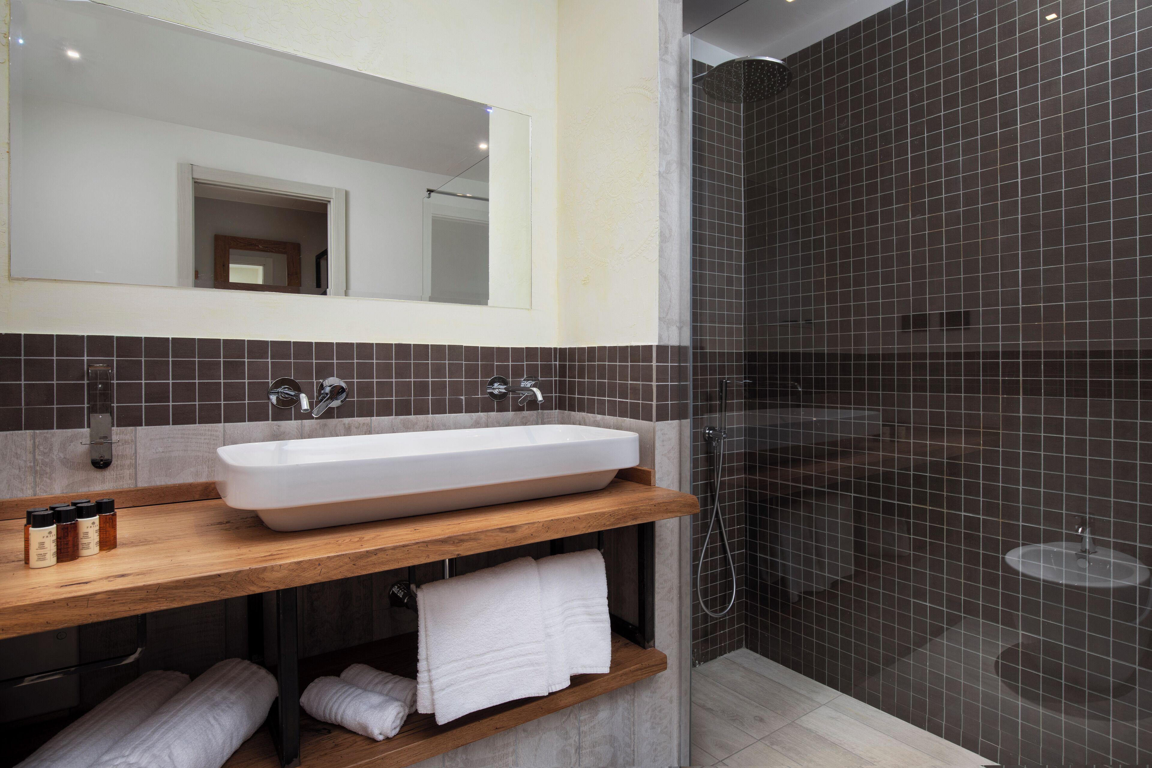 Un bagno moderno con un lavandino bianco grande, un mobile bagno in legno e uno spazio doccia con pareti in vetro.