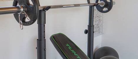 A home gym with a bench press, barbell, and weight plates.