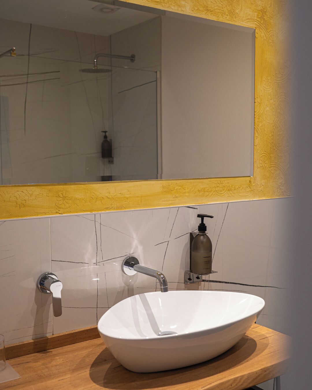 A bathroom with a white sink, a mirror with a yellow frame, and a shower visible in the reflection.