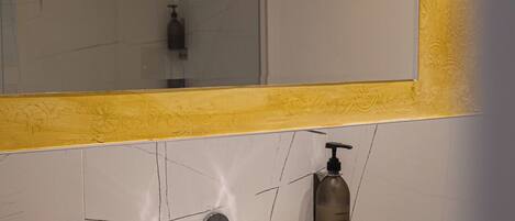 A bathroom with a white sink, a mirror with a yellow frame, and a shower visible in the reflection.
