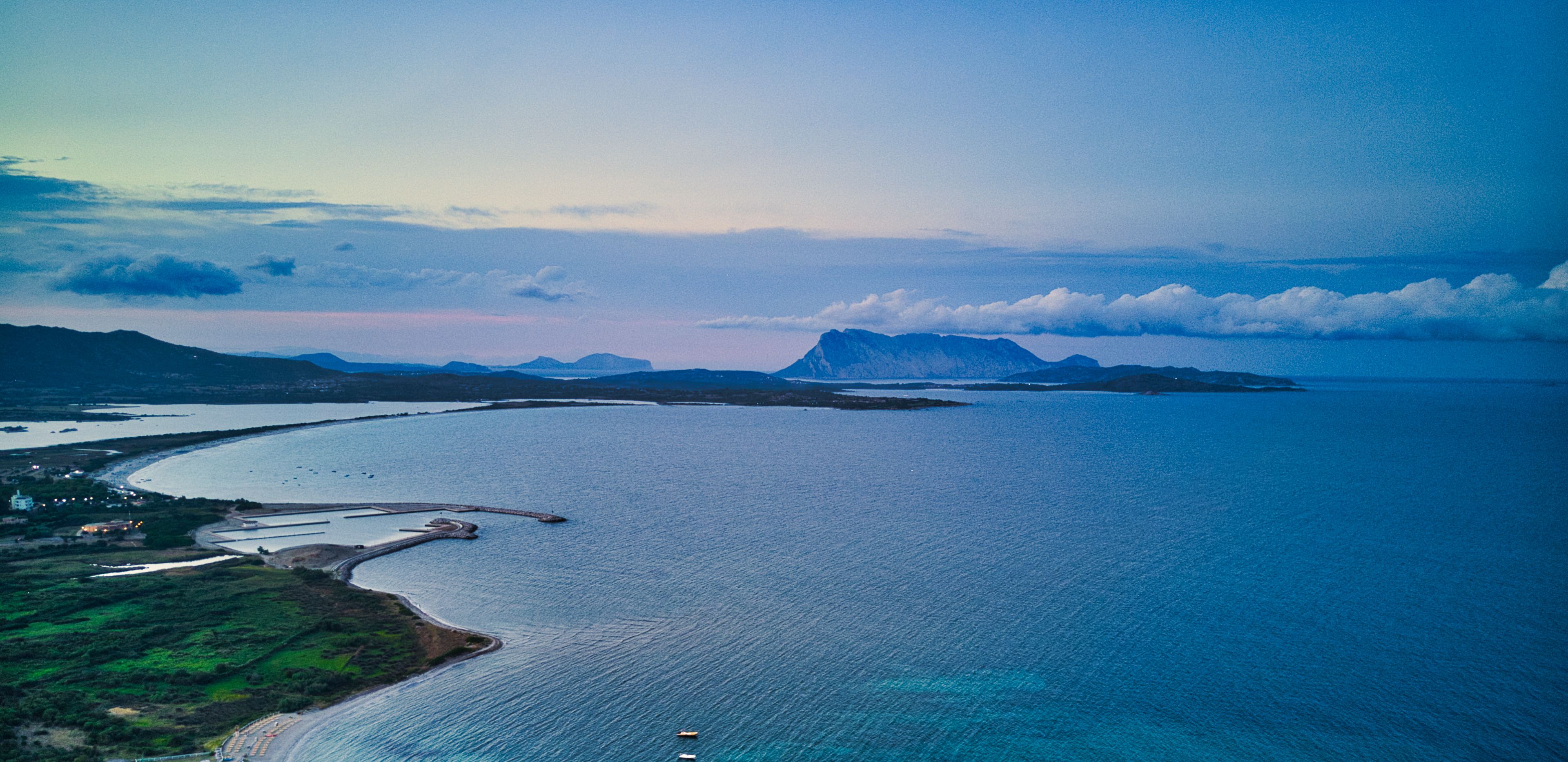 An aerial view of a coastal area with a large body of water, a peninsula, and distant mountains.