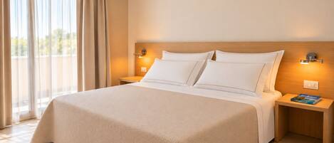 Habitación de hotel con una cama grande, dos mesitas de noche y vistas al exterior a través de una ventana con cortinas.