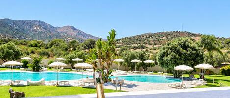 A table with a bottle of wine and two glasses, overlooking a pool and a mountainous landscape.