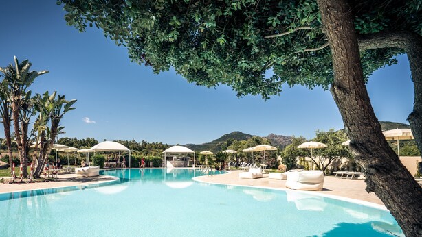 A swimming pool with lounge chairs and umbrellas, surrounded by trees and a mountain in the background. - Hotel San Teodoro (San Teodoro)
