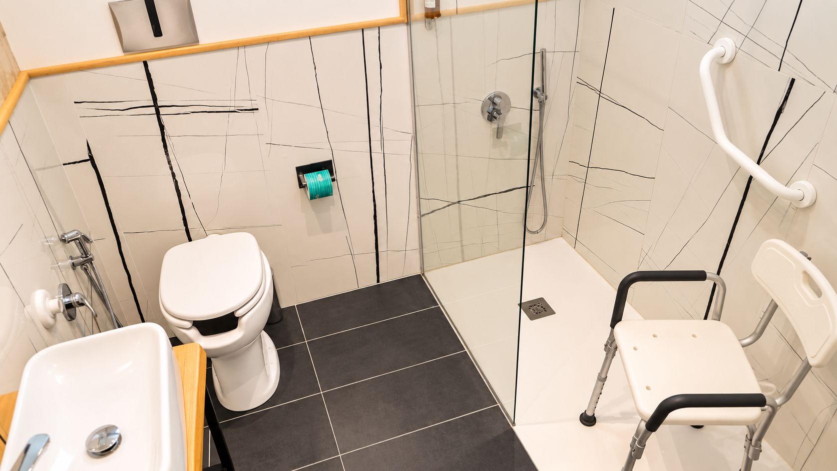 Een badkamer met toilet, douche en een rolstoeltoegankige stoel.
