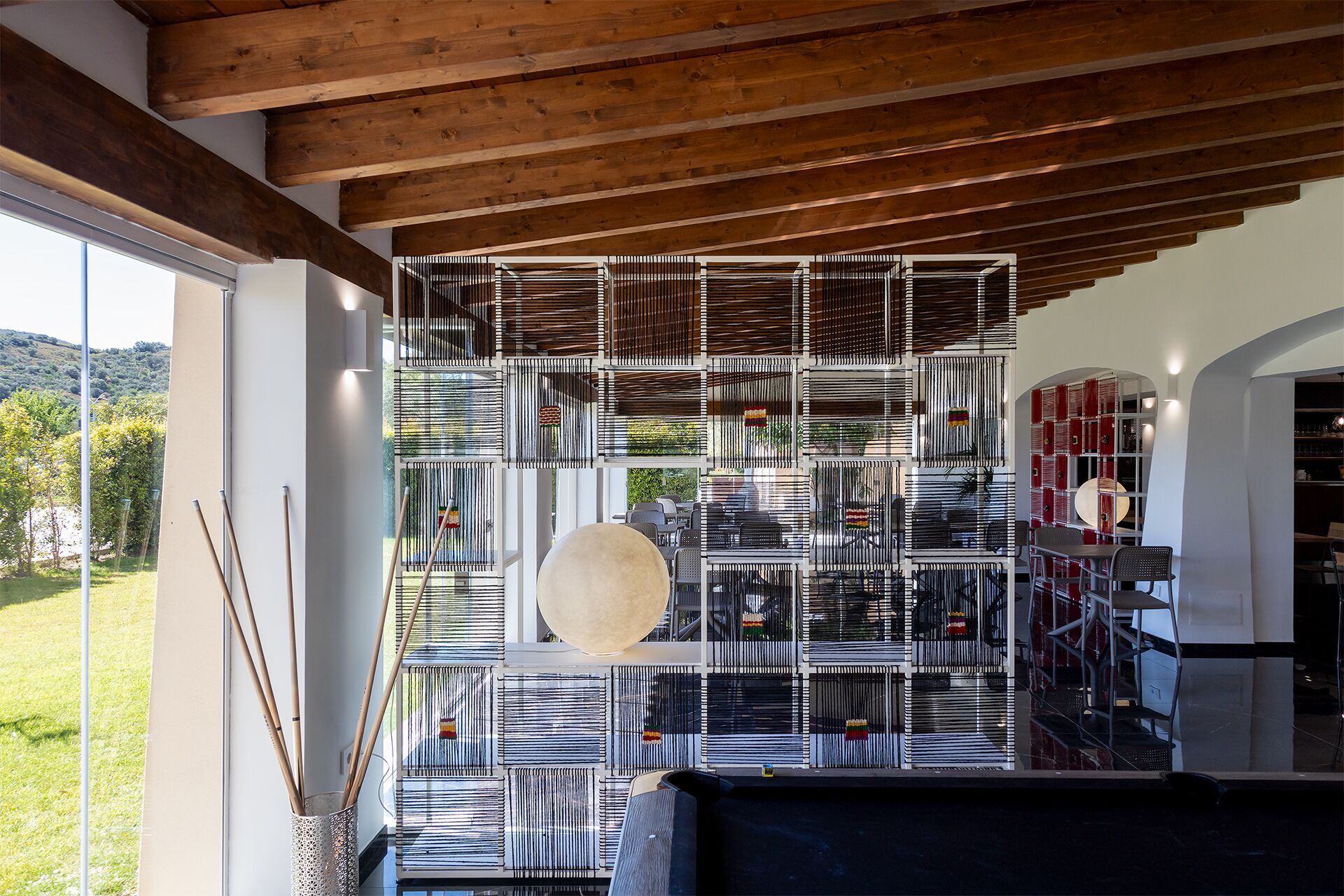A modern interior with a wooden ceiling, a large window overlooking a green landscape, and a unique wall design with vertical slats.