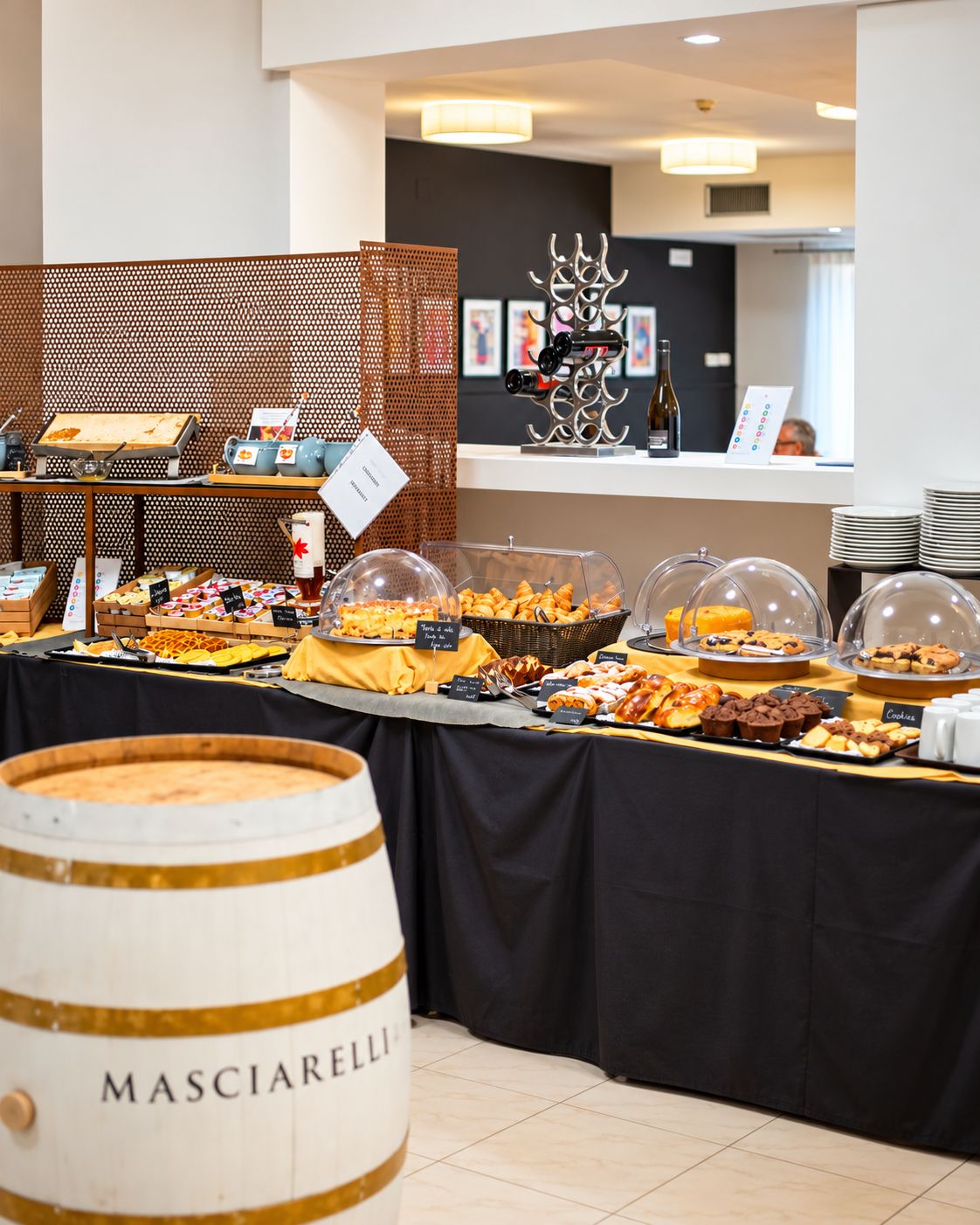 Montaje de buffet con diferentes alimentos, una botella de vino y un barril con la etiqueta 'MASCIARRELLI'.