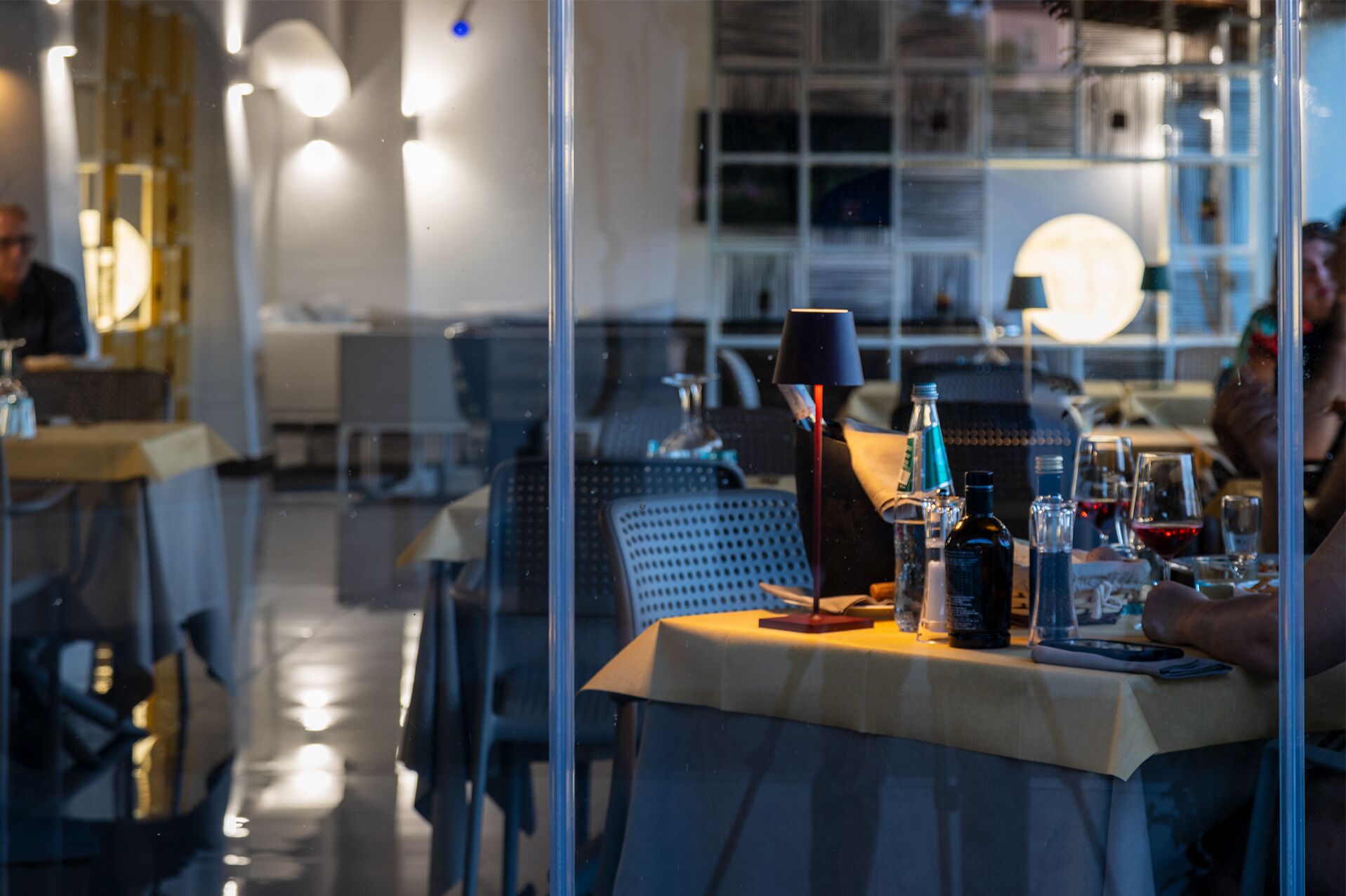 Un interior de restaurante con mesas, sillas y una variedad de botellas y vasos sobre las mesas.