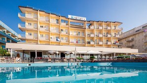 A multi-story hotel with a swimming pool, outdoor seating, and balconies. - Hotel Astor (Jesolo)