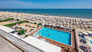 Una grande piscina circondata da ombrelloni e lettini, con vista sulla spiaggia e sull'oceano.