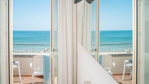 A balcony with a view of the sea, white chairs, and a glass door. - Hotel Astor (Jesolo)