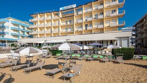 Un hotel con diversi balconi, arredi sulla spiaggia e ombrelloni.
