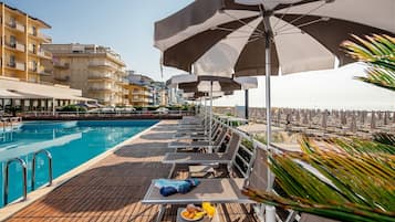 A poolside area with lounge chairs, umbrellas, and a dining table with food and drinks.