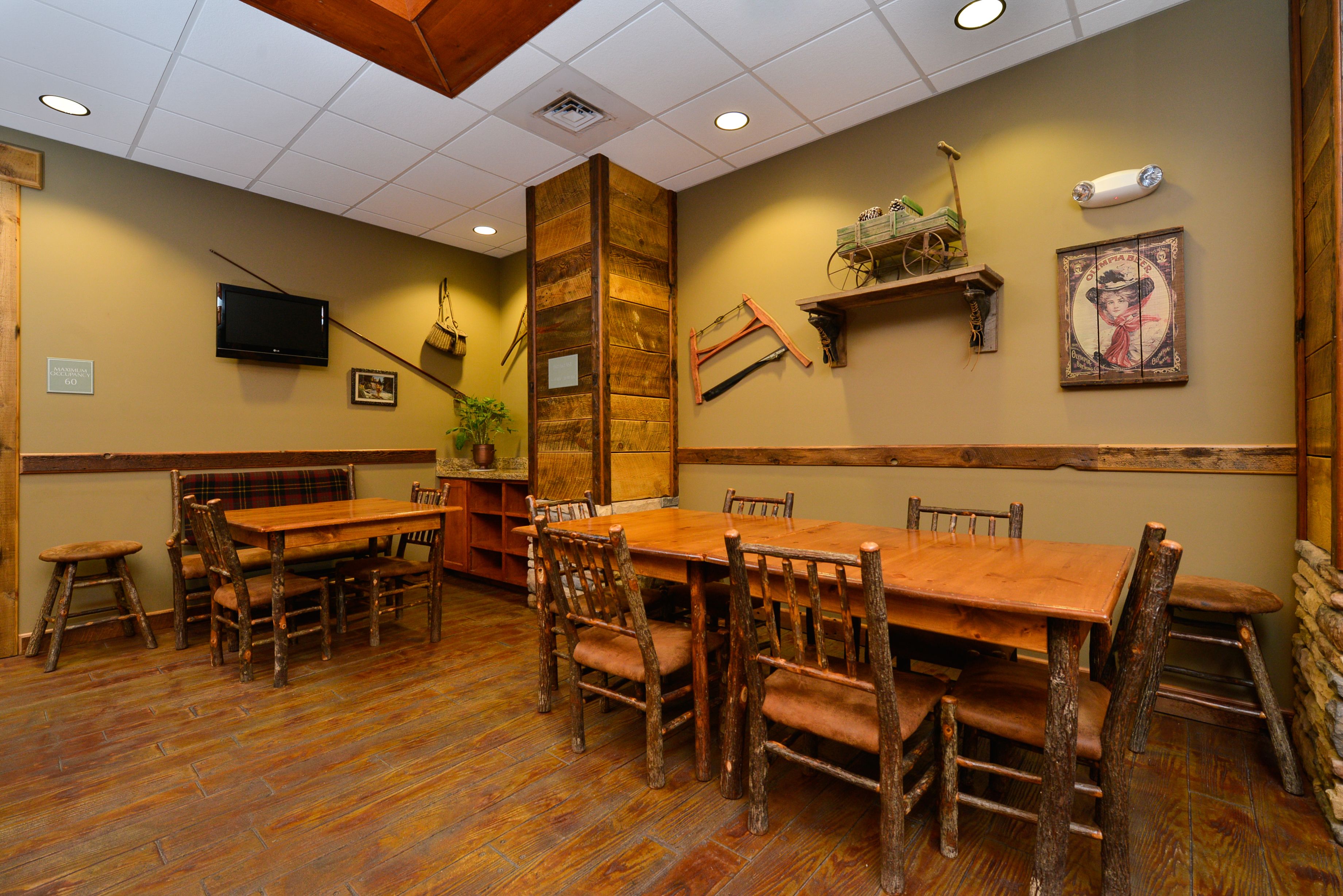 A rustic dining area with wooden tables and chairs, a television mounted on the wall, and a wooden accent wall.
