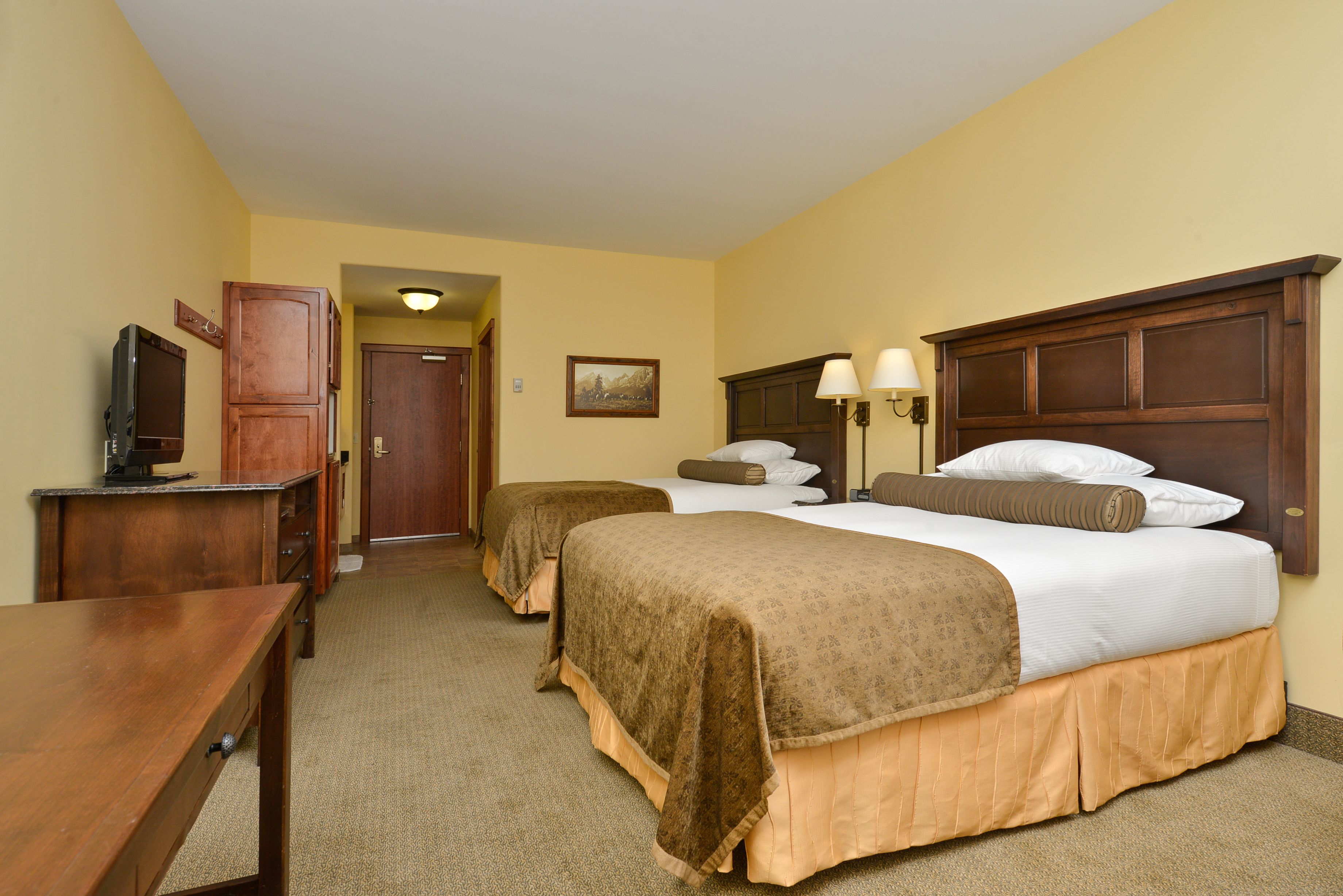 A hotel room with two beds, a desk, a television, and a door leading to another room.