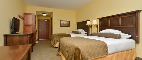 A hotel room with two beds, a desk, a television, and a door leading to another room.