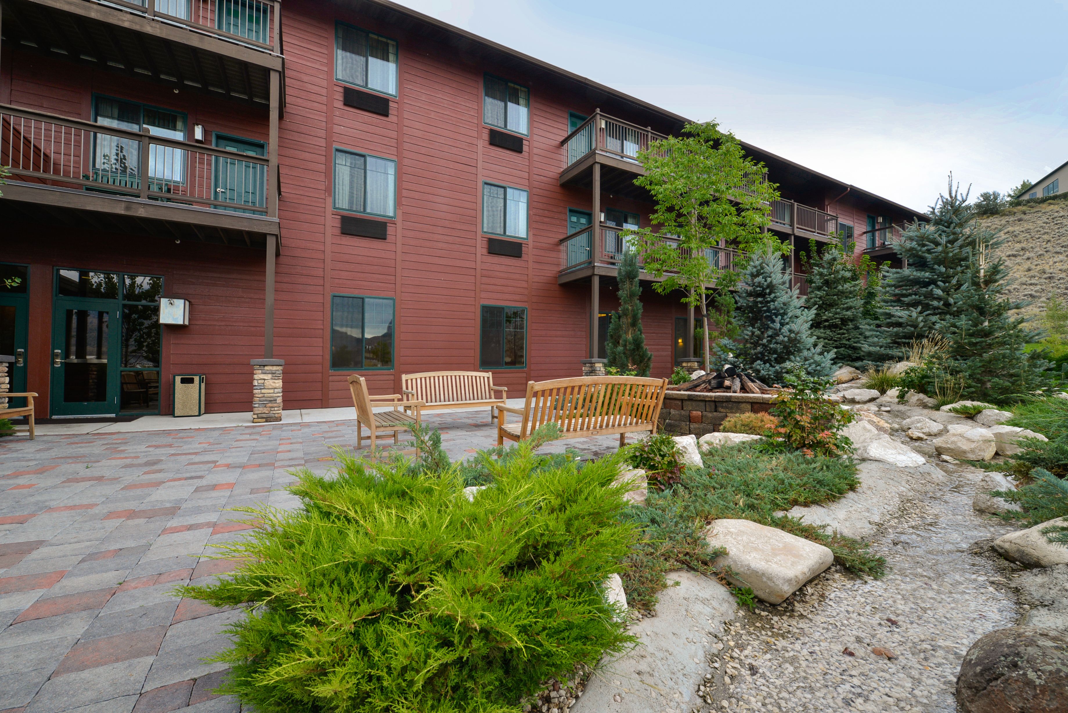 A multi-story building with balconies, outdoor seating, and a landscaped garden area.