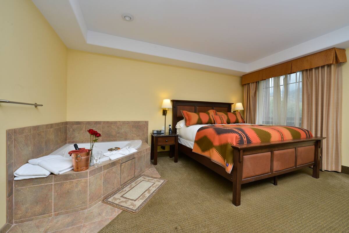 A hotel room with a large bed, a separate bathtub, and a nightstand with lamps.