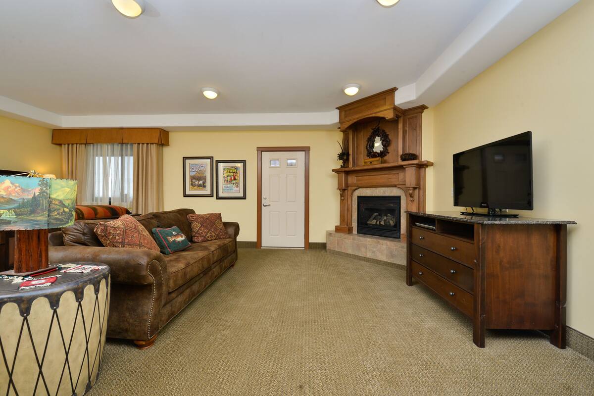 A living room with a brown leather sofa, a wooden entertainment center, a fireplace, and a television.