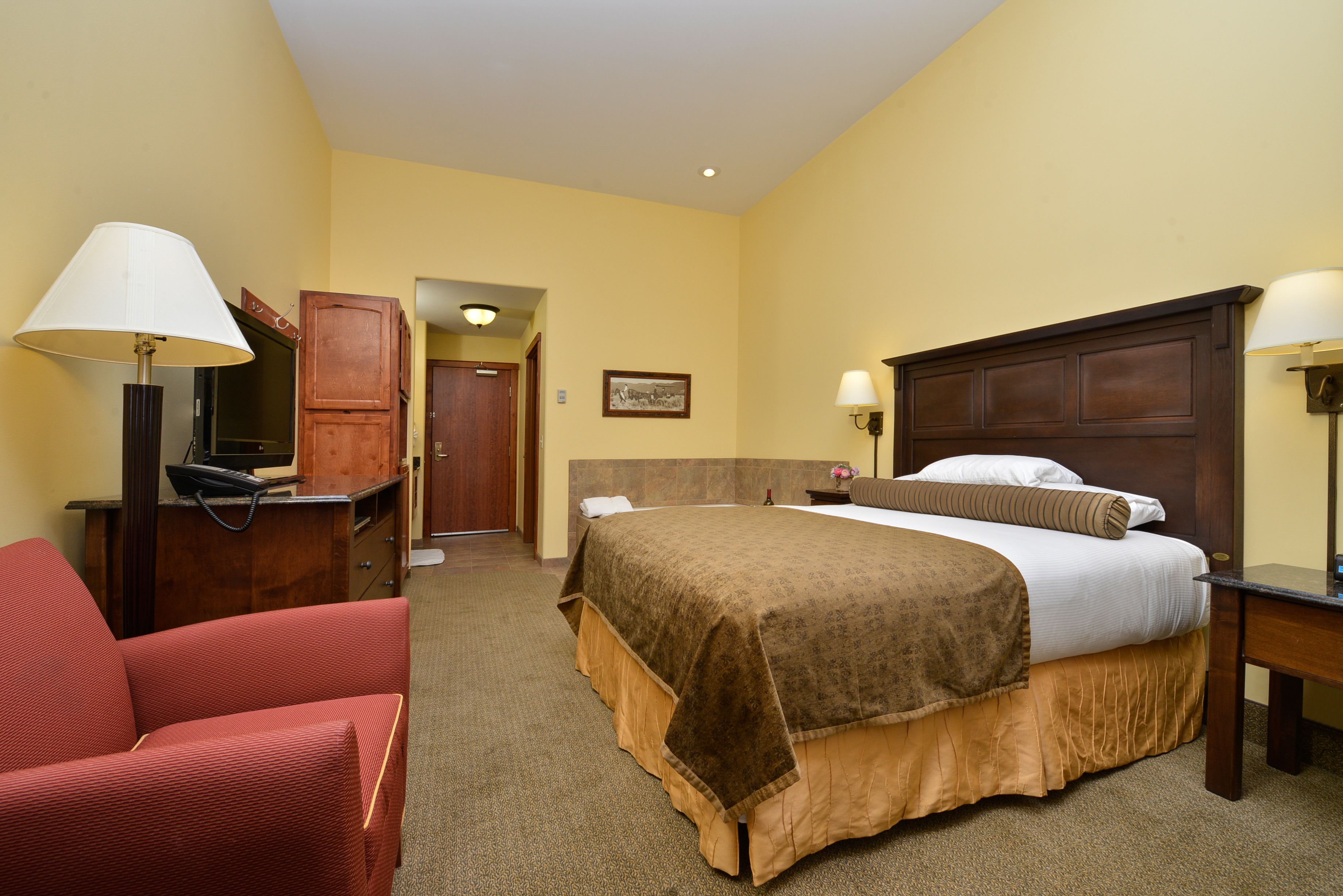 A hotel room with a bed, a desk, a chair, and a lamp.