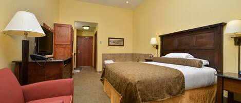 A hotel room with a bed, a desk, a chair, and a lamp.